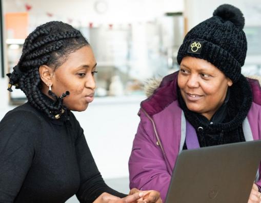 Image of two individuals sat in front of laptop, one offering guidance to the other